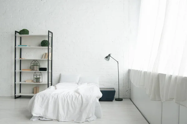 Interior del acogedor dormitorio con almohadas en la cama, mesita de noche, lámpara y rack - foto de stock