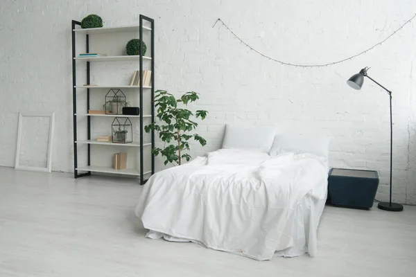 Intérieur de la chambre avec oreillers sur le lit, table de chevet, lampe, cadre photo et rack — Photo de stock