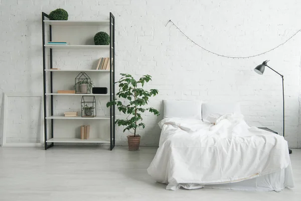 Intérieur de la chambre confortable avec des oreillers sur le lit, table de chevet, lampe, cadre photo et rack — Photo de stock