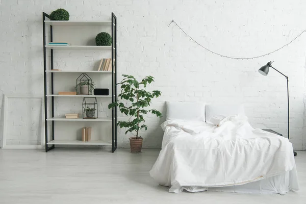 Interior do quarto acolhedor com travesseiros na cama, mesa de cabeceira, lâmpada, moldura e rack — Fotografia de Stock