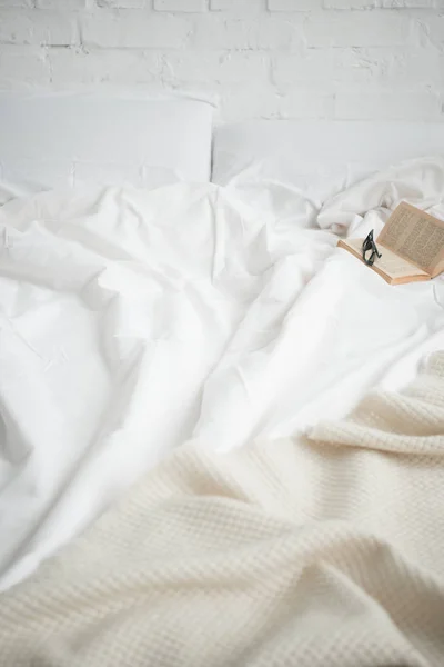 Book and glasses on empty cozy white bed — Stock Photo