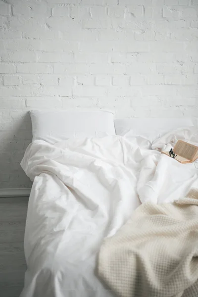 Brille und Buch auf dem Bett mit weißer Decke und Kissen — Stockfoto