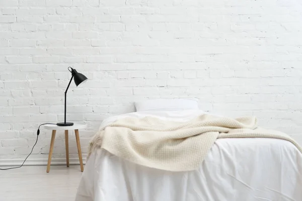 Interior del acogedor dormitorio con almohada en la cama y lámpara en el taburete - foto de stock