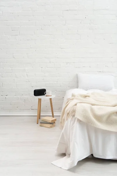 Innenraum des gemütlichen Schlafzimmers mit Büchern, Kissen auf dem Bett, Wecker und Kaffeetasse auf Hocker — Stockfoto