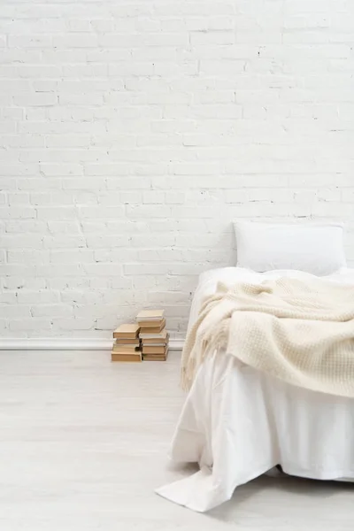 Chambre avec oreiller blanc sur lit vide et livres sur le sol — Photo de stock
