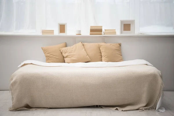 Interior of bedroom with brown pillows on bed, books, coffee cup and photo frames — Stock Photo