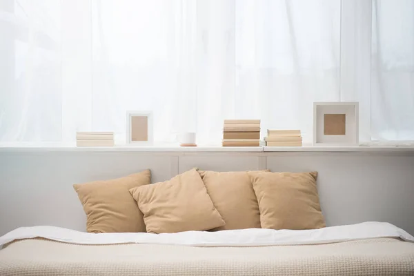 Bedroom with brown pillows on bed, books, coffee cup and photo frames — Stock Photo