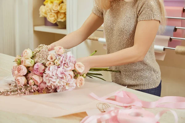 Vista recortada de floristería envolviendo ramo de rosas y peonías en el espacio de trabajo - foto de stock