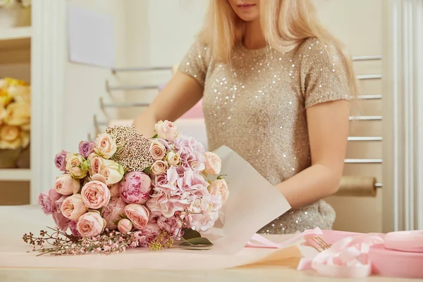 Teilansicht des Blumenhändlers, der einen Strauß Rosen und Pfingstrosen am Arbeitsplatz einwickelt — Stockfoto