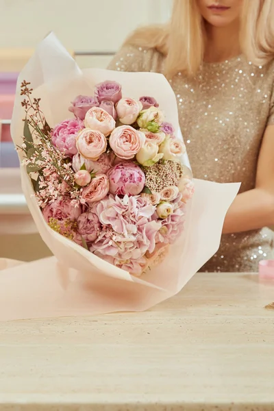 Partial view of florist wrapping with paper bouquet of roses and peonies at workspace — Stock Photo