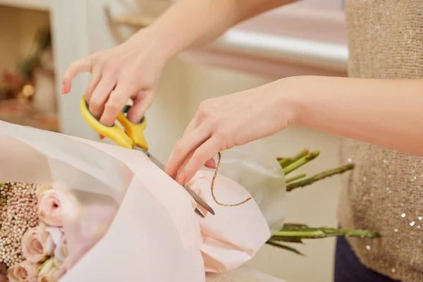 Partial view of florist cutting strip with scissors on bouquet — Stock Photo