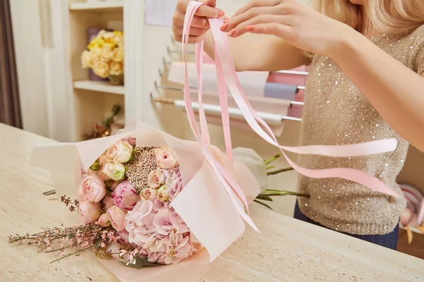 Partial view of florist tying ribbons on bouquet of roses and peonies — Stock Photo