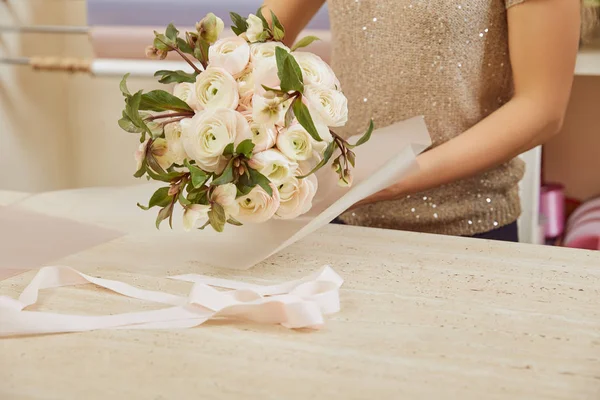 Vista cortada de florista embrulhando buquê de peônias brancas no espaço de trabalho — Fotografia de Stock
