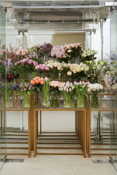 Rosas, tulipanes y peonías en jarrones sobre mesas de cristal - foto de stock