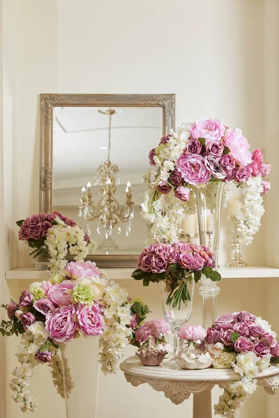 Espejo, flores blancas y moradas en jarrones de vidrio en la mesa y estante - foto de stock