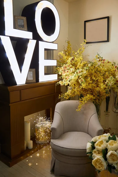 Interior de la habitación con sillón, iluminación con letras de amor y flores amarillas - foto de stock