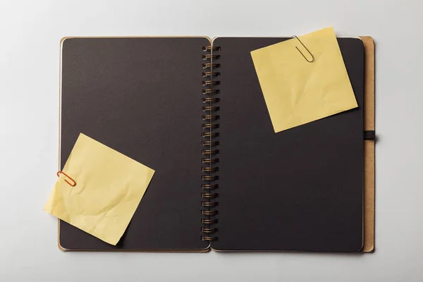 Top view of opened notebook with black sheets and sticky notes with paper clips on white background — Stock Photo