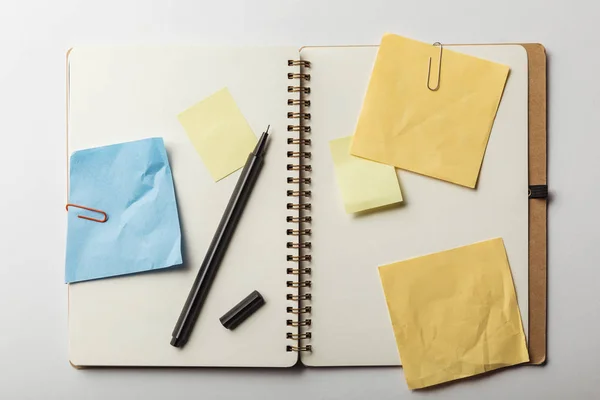 Vue du haut du carnet ouvert avec notes collantes bleues et jaunes avec trombones sur fond blanc — Photo de stock