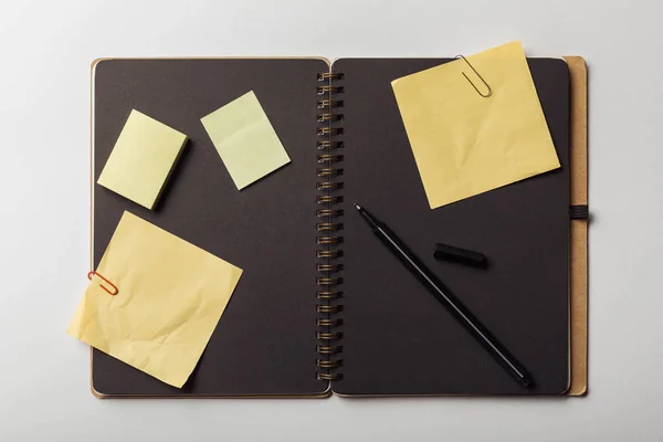 Vue du haut du carnet ouvert avec feuilles noires et notes collantes jaunes avec trombones sur fond blanc — Photo de stock