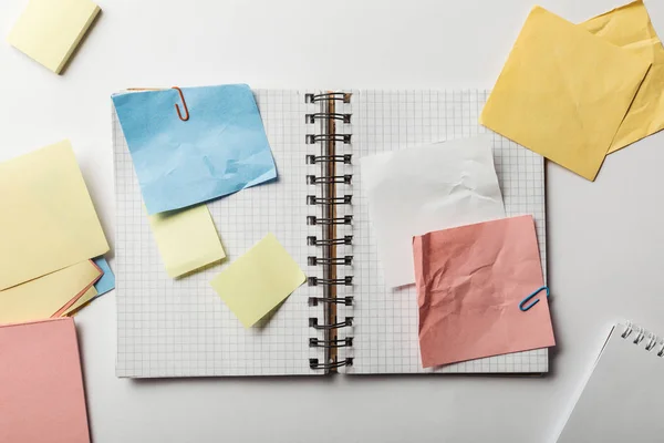 Vue du haut du carnet ouvert avec des papiers carrés et des notes collantes froissées sur fond blanc — Photo de stock