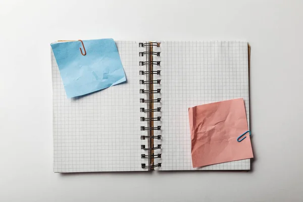 Vista superior del cuaderno abierto con papeles cuadrados y notas adhesivas azul y rosa arrugadas sobre fondo blanco — Stock Photo