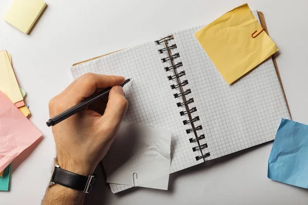 Vista recortada del hombre sosteniendo pluma cerca de páginas cuadradas en cuaderno cerca de notas pegajosas arrugadas — Stock Photo