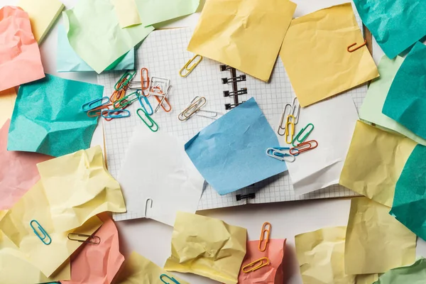 Vue du haut du carnet ouvert avec des papiers carrés près de notes collantes froissées et des trombones colorés — Photo de stock