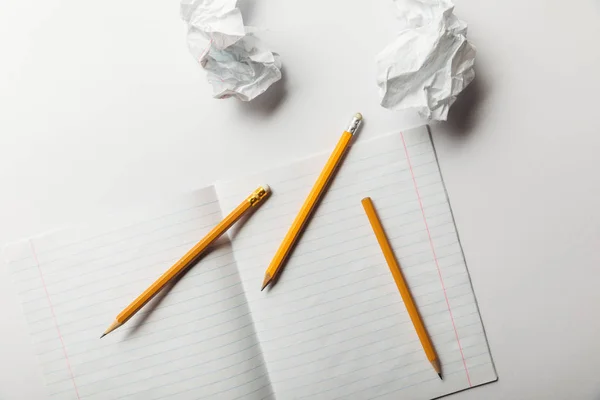 Vue du haut de la feuille vierge tapissée située près des papiers froissés et des crayons sur fond blanc — Photo de stock