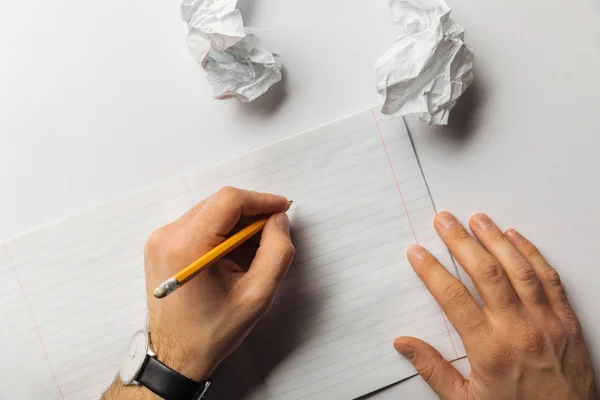 Обрезанный вид человека, пишущего на пустом листе возле скомканных бумаг на белом фоне — стоковое фото