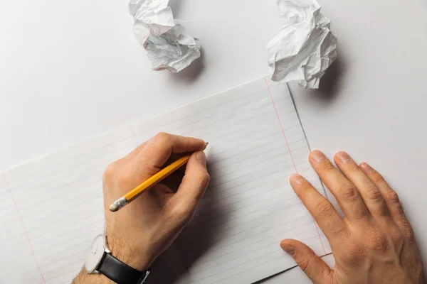 Vue recadrée de l'homme écrivant sur une feuille blanche près de papiers froissés sur fond blanc — Photo de stock