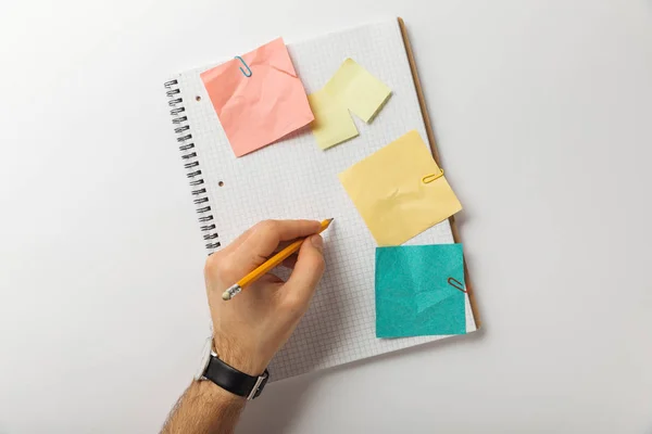 Vista recortada del hombre escribiendo en hoja cuadrada en blanco cerca de palos de papel arrugado sobre fondo blanco — Stock Photo