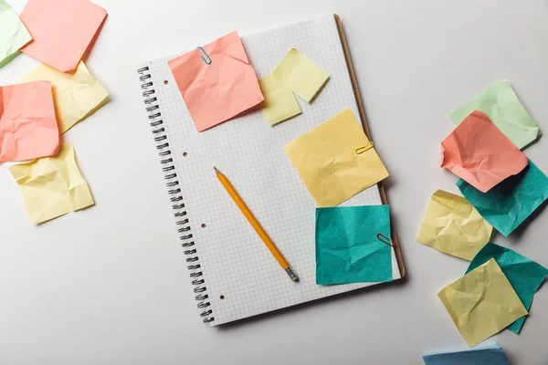 Vista superior del cuaderno con la página cuadrada en blanco cerca de notas pegajosas coloridas arrugadas sobre fondo blanco — Stock Photo