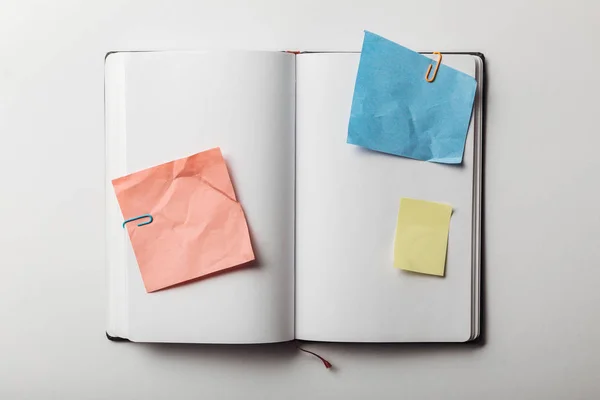 Top view of opened notebook with blue, pink and yellow sticky notes with paper clips on white background — Stock Photo