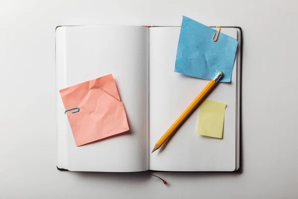 Top view of opened notebook with sticky notes and paper clips near pencil on white background — Stock Photo
