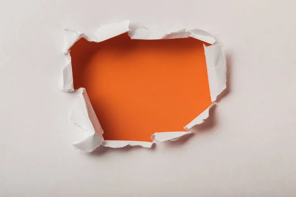 Agujero roto en hoja de papel sobre fondo naranja - foto de stock