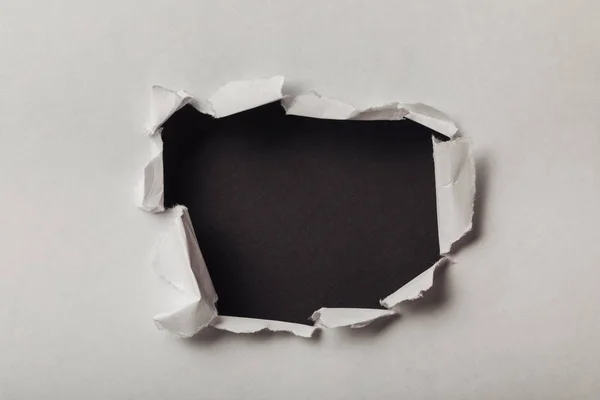 Trou déchiré dans une feuille de papier sur fond noir — Photo de stock