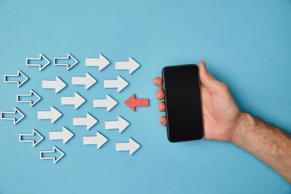 Cropped view of man holding smartphone over red horizontal pointer opposite white arrows on blue background — Stock Photo