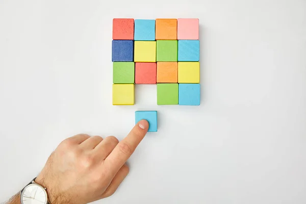 Обрізаний вид чоловічої руки, що кладе кубик на набір різнокольорових блоків на сірому фоні — стокове фото