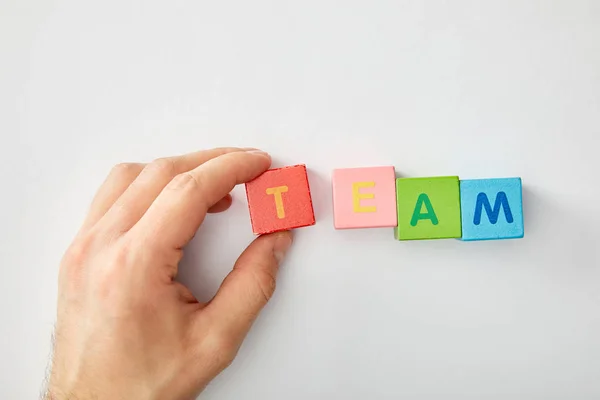 Cropped view of man making team lettering of multicolored cubes on grey background — Stock Photo