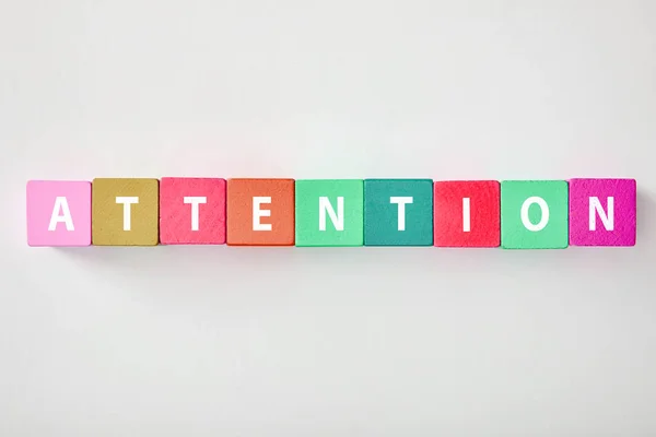 Top view of attention lettering made of multicolored cubes on grey background — Stock Photo