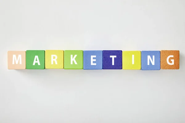 Top view of marketing lettering made of multicolored cubes on grey background — Stock Photo