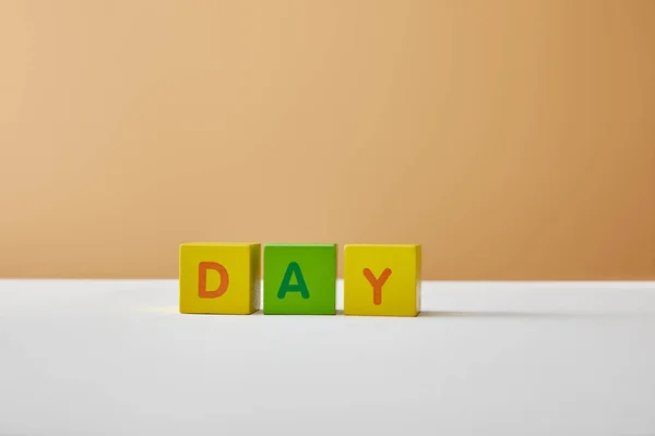 Letras de día hechas de bloques multicolores sobre mesa blanca y fondo beige - foto de stock