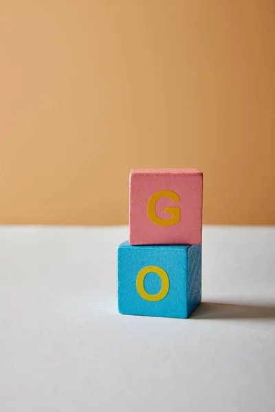 Вертикальный идти буквы из разноцветных блоков на белом столе и бежевом фоне — стоковое фото