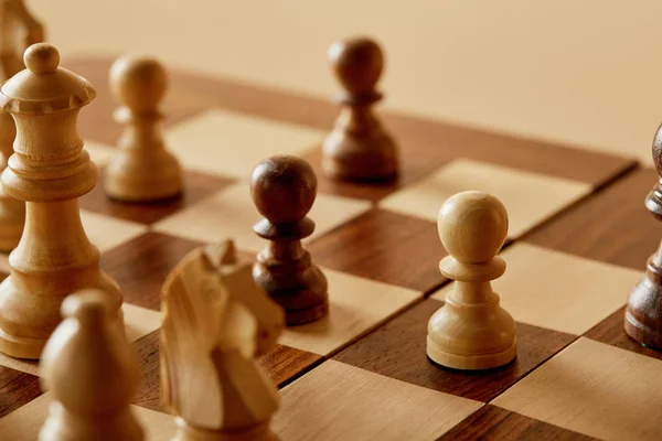 Enfoque selectivo de piezas de ajedrez sobre tablero de ajedrez marrón de madera y fondo beige - foto de stock