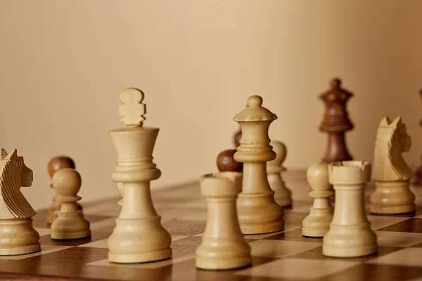 Selective focus of chess pieces on brown chess board and beige background — Stock Photo