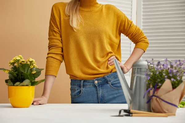 Vista recortada de la mujer de pie cerca de la mesa con flores y regadera - foto de stock