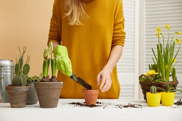 Partial view of gardener in sweater filling flowerpot with spade — Stock Photo