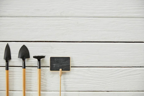 Top view of spades, rake and empty board on white table — Stock Photo