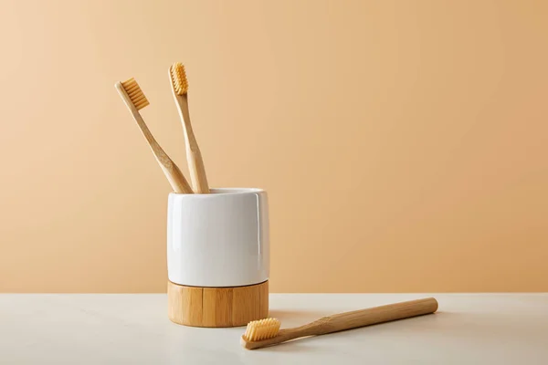 Bamboo toothbrushes and holder on white table and beige background — Stock Photo