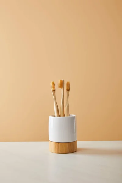 Escovas de dentes de bambu em suporte na mesa branca e fundo bege — Fotografia de Stock